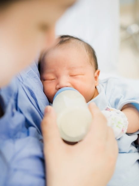 mother holding infant feeding with bottle of milk