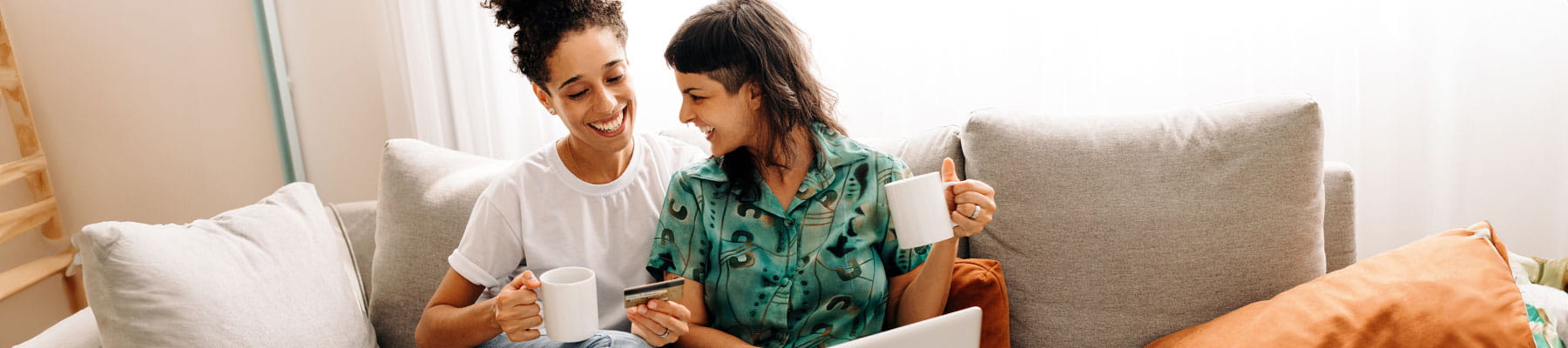 Two women pay their bills from the couch