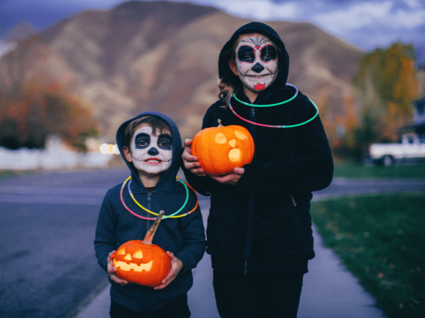 Children trick or treating wearing costumes and glow sticks while holding pumpkins