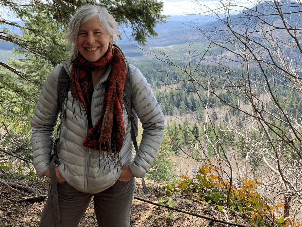 Wendy Berger, wearing a gray coat and red scarf, posing in front of a valley