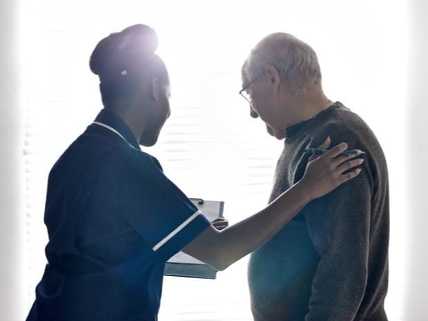 photo of healthcare worker holding a clipboard with a form on it, with their spare hand on an elderly patient's shoulder