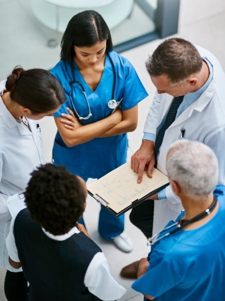 photo looking down at five healthcare workers huddled in a circle looking at a clipboard with a form on it held by one of the healthcare workers