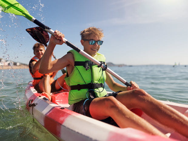 Photo of two young children wearing PFD life jackets paddling on a lake in a kayak